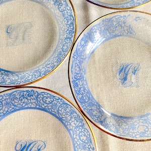 May include: Four clear glass plates with a blue and gold design. Each plate has a gold rim and a blue floral pattern. The plates are monogrammed with the letters "W.G."