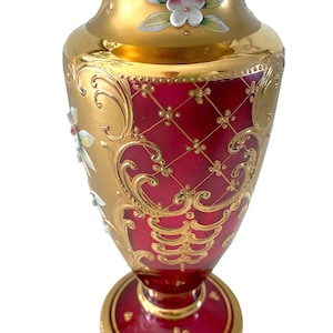 May include: A red glass vase with gold painted details and floral designs. The vase has a wide mouth and a round base.