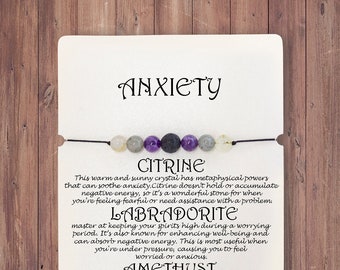 Könnte beinhalten: Eine Karte mit dem Wort "Angst" obenauf. Die Karte listet die Eigenschaften der Kristalle Citrin, Labradorit, Amethyst und Lavastein auf. Die Karte zeigt auch ein Armband mit den Kristallen.