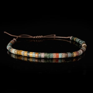May include: A multi-colored beaded bracelet with a brown cord. The beads are made of various shades of green, brown, yellow, and red.