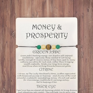 May include: A bracelet with green jade, citrine, and tiger's eye beads. The bracelet is on a white card with the text "Money & Prosperity" and descriptions of the stones' properties.