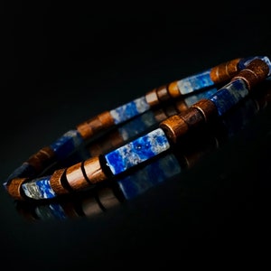 May include: A bracelet featuring alternating blue lapis lazuli and wooden beads. The blue beads are rectangular and the wooden beads are cylindrical. The bracelet is strung on a flexible cord, creating a stylish accessory.