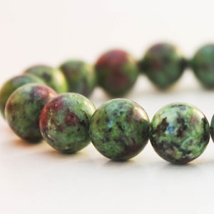 May include: A green and red gemstone bracelet with round beads. The beads have a mottled pattern.