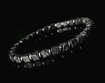 May include: A black lava rock bracelet with silver accents. The bracelet is made of square-shaped beads and is designed to be worn on the wrist.