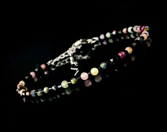 May include: A multi-coloured gemstone bracelet with a silver clasp. The bracelet features round beads in shades of pink, green, yellow, and black.