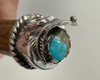 May include: A silver cap featuring a round, bright blue turquoise stone set in a serrated bezel. The silver base is decorated with a twisted rope border, stamped star and crescent moon symbols, and a curved, leaf-like metal accent piece.