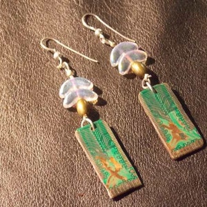 May include: A pair of earrings with green circuit board pendants and iridescent white flower accents. The earrings are made with gold-toned metal and have silver hooks.