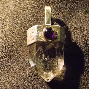 May include: A silver pendant with a clear quartz crystal point and a purple amethyst stone set in the center.
