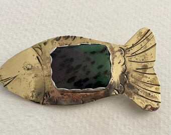 May include: A fish-shaped brooch crafted from brass with a weathered, golden-toned surface. The center features a rectangular, polished stone inlay in shades of deep forest green and black, secured within a silver-toned metal bezel setting.