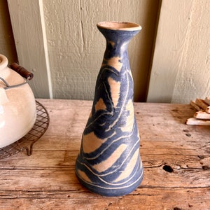 May include: A blue and white ceramic vase with a wavy design. The vase has a narrow neck and a wide base.