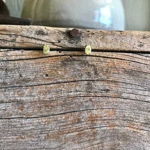 May include: A pair of oval-shaped yellow gemstone earrings on a rustic wooden surface.