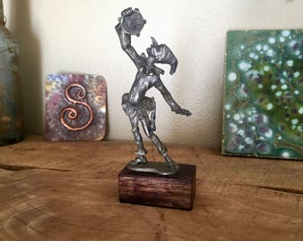 May include: A pewter figurine of a jester holding a tambourine. The figurine is standing on a dark wood base.