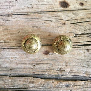 May include: A pair of gold-toned clip-on earrings with a textured, circular design.
