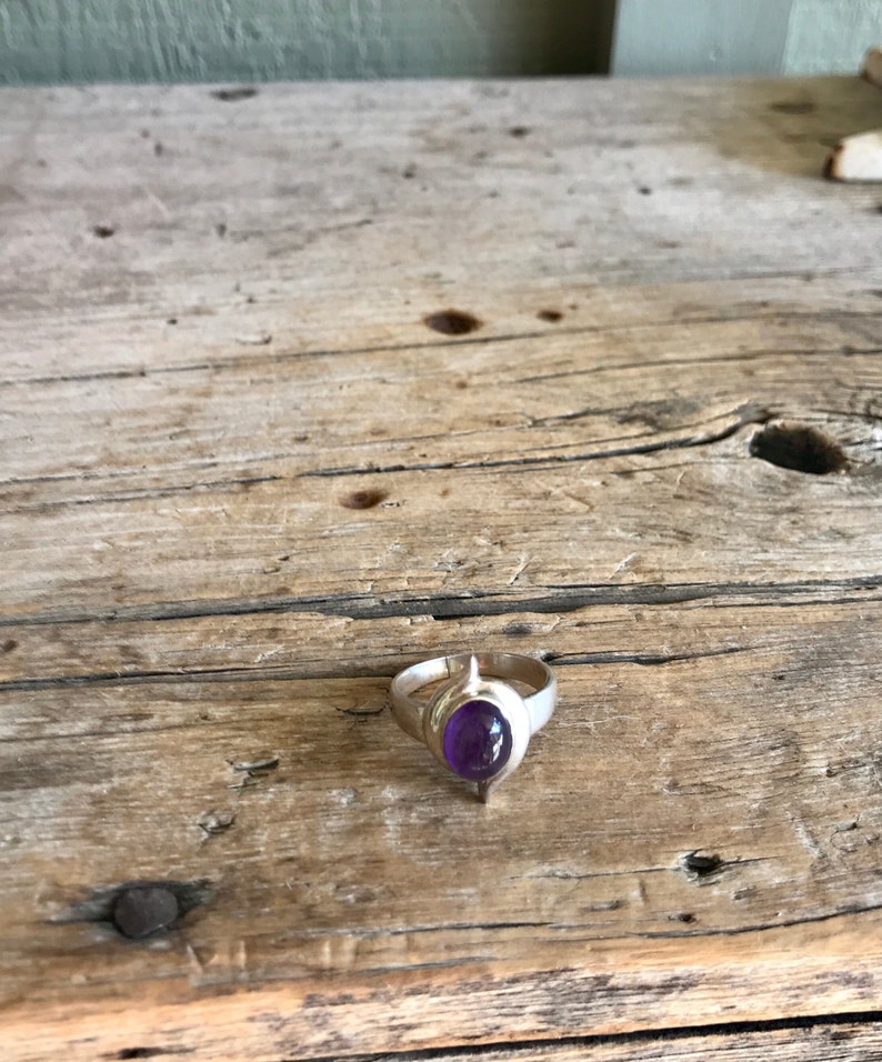May include: A silver ring with a purple amethyst gemstone set in a pointed, leaf-shaped design.