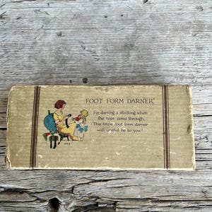 May include: Vintage "Foot Form Darner" box with an illustration of two girls. The box is rectangular with text that reads "For darning a stocking when the toes come through." The box is tan with brown vertical stripes.