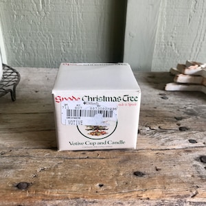 May include: A white box with a green and red Christmas tree design. The box says "Spode Christmas Tree" and "Votive Cup and Candle". The box has a barcode and the text "Dillard's" on it.