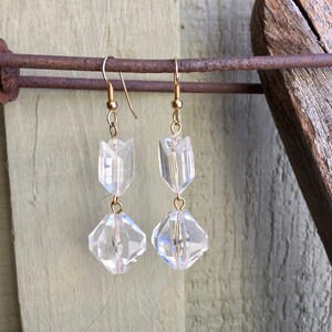 May include: A pair of gold dangle earrings with clear faceted glass beads. The earrings are hanging from a rusty metal bar.