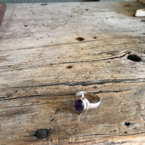 May include: A silver ring with a purple amethyst gemstone set in a simple oval shape.