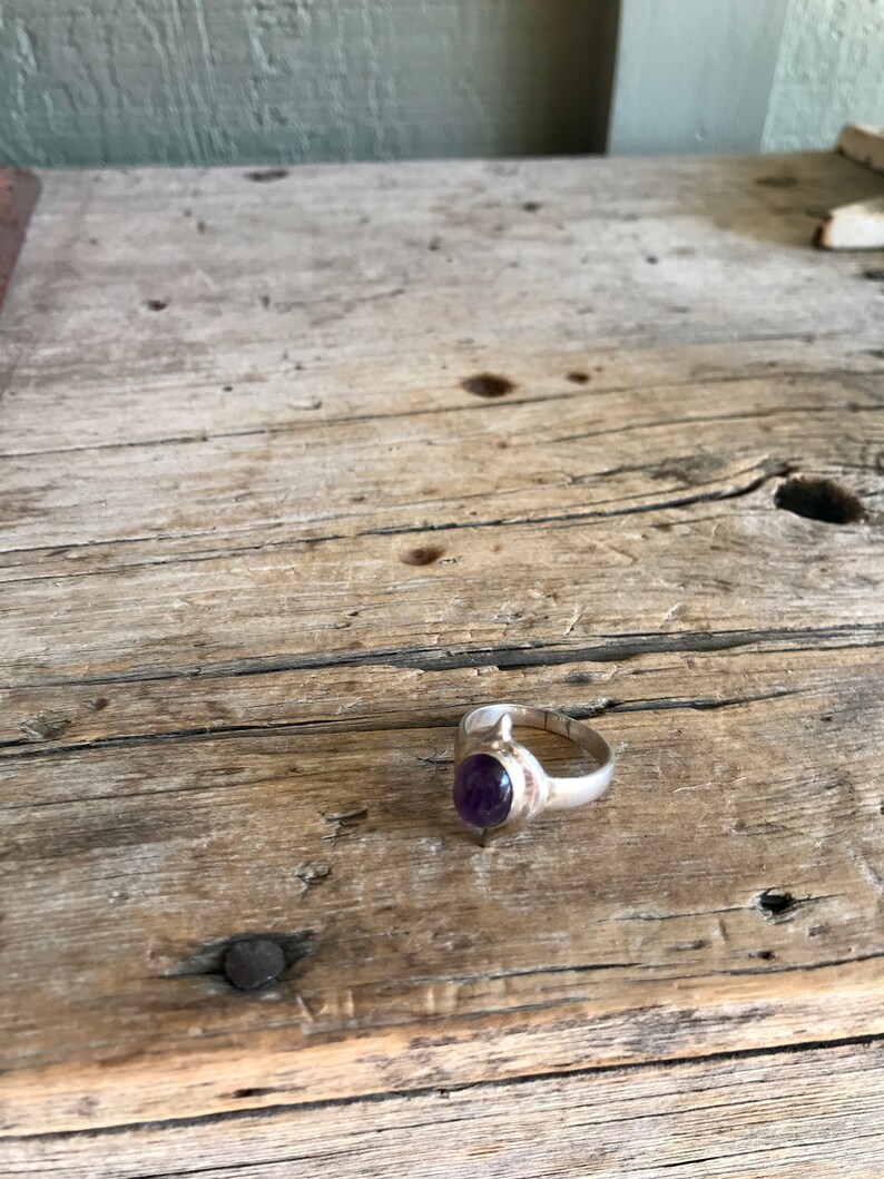 May include: A silver ring with a purple amethyst gemstone set in a simple oval shape.