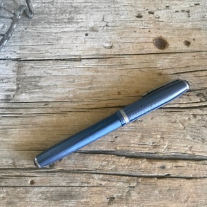 May include: A blue pen with a silver trim lies on a weathered wooden surface.