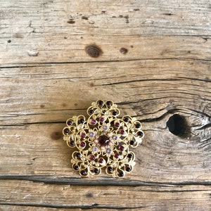 May include: A gold-toned brooch with a floral design and purple and pink rhinestones.