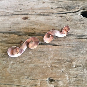 May include: A pair of vintage copper earrings with a swirling design. The earrings are made of a thin, flat piece of copper that has been twisted and shaped into a spiral.