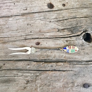 May include: Silver souvenir fork with a red, white, and blue enamel design featuring the Canadian coat of arms. The handle is inscribed with the word "CANADA".