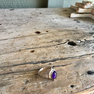 May include: A silver ring with a purple gemstone set in a teardrop shape.
