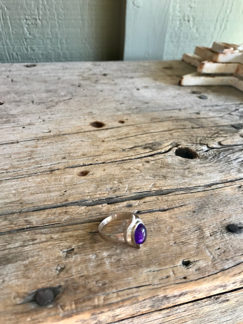 May include: A silver ring with a purple gemstone set in a teardrop shape.