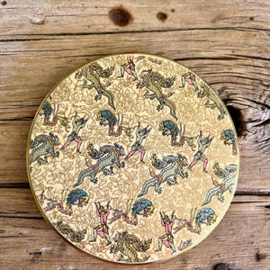 May include: Round, cream-coloured trinket box with a gold rim. The lid features a repeating pattern of green and blue dragons with pink and yellow figures.