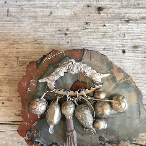 May include: A silver charm bracelet with a bird-shaped pendant and multiple silver bells and charms. The bracelet is displayed on a wooden surface.