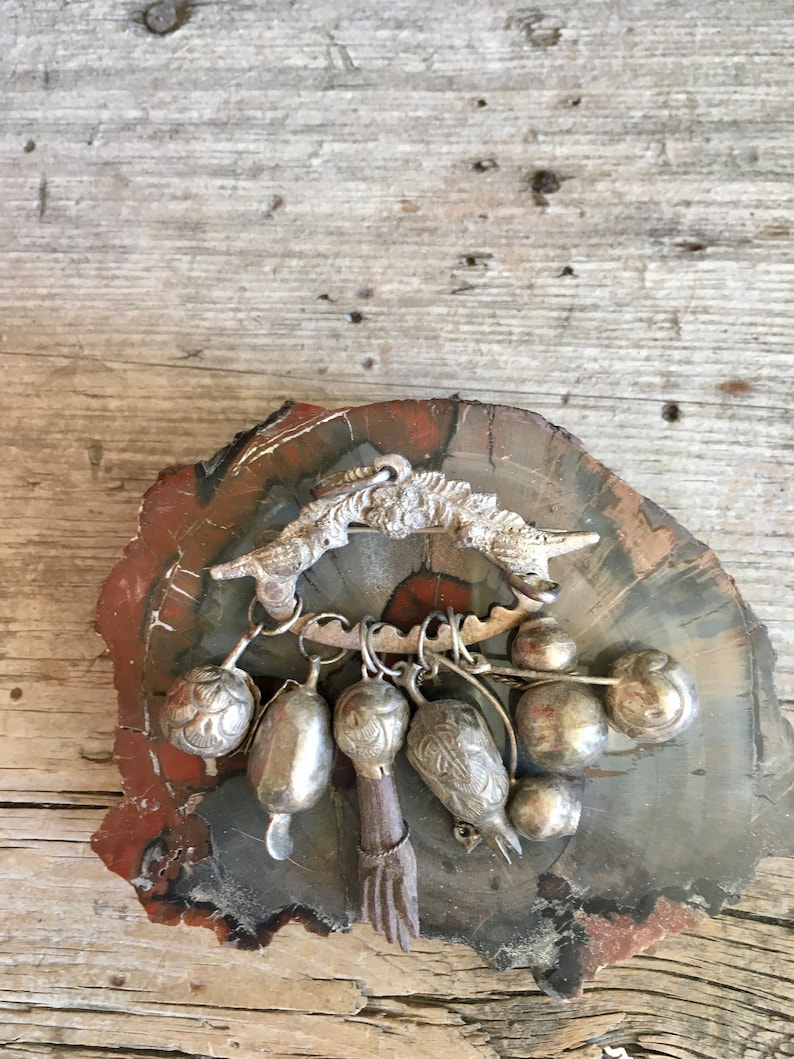 May include: A silver charm bracelet with a bird-shaped pendant and multiple silver bells and charms. The bracelet is displayed on a wooden surface.