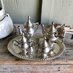 May include: A silver tea set with a teapot, creamer, and sugar bowl on a silver tray. The set is on a wooden surface.