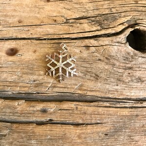 May include: A gold snowflake charm with clear crystals. The charm is on a wooden surface.