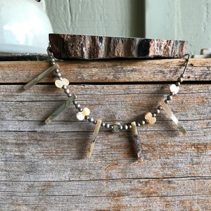 May include: A silver necklace with a series of small, round, white beads and dangling, rectangular, iridescent shell pieces. The necklace is displayed on a wooden surface.