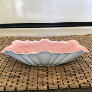 May include: A light pink and gray ceramic bowl with a scalloped edge. The bowl is shaped like a flower and has a glossy finish.