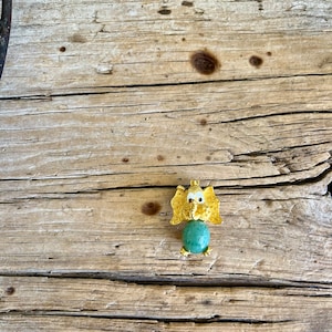 May include: A gold-colored elephant figurine with a green gemstone body. The elephant has large, white eyes and a small, gold trunk.