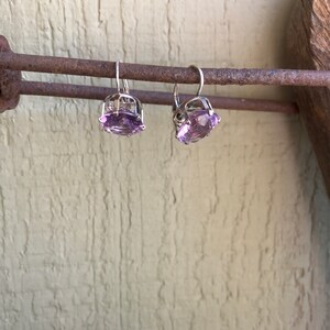 May include: A pair of silver earrings with amethyst gemstones. The earrings are hanging from a rusty metal bar.