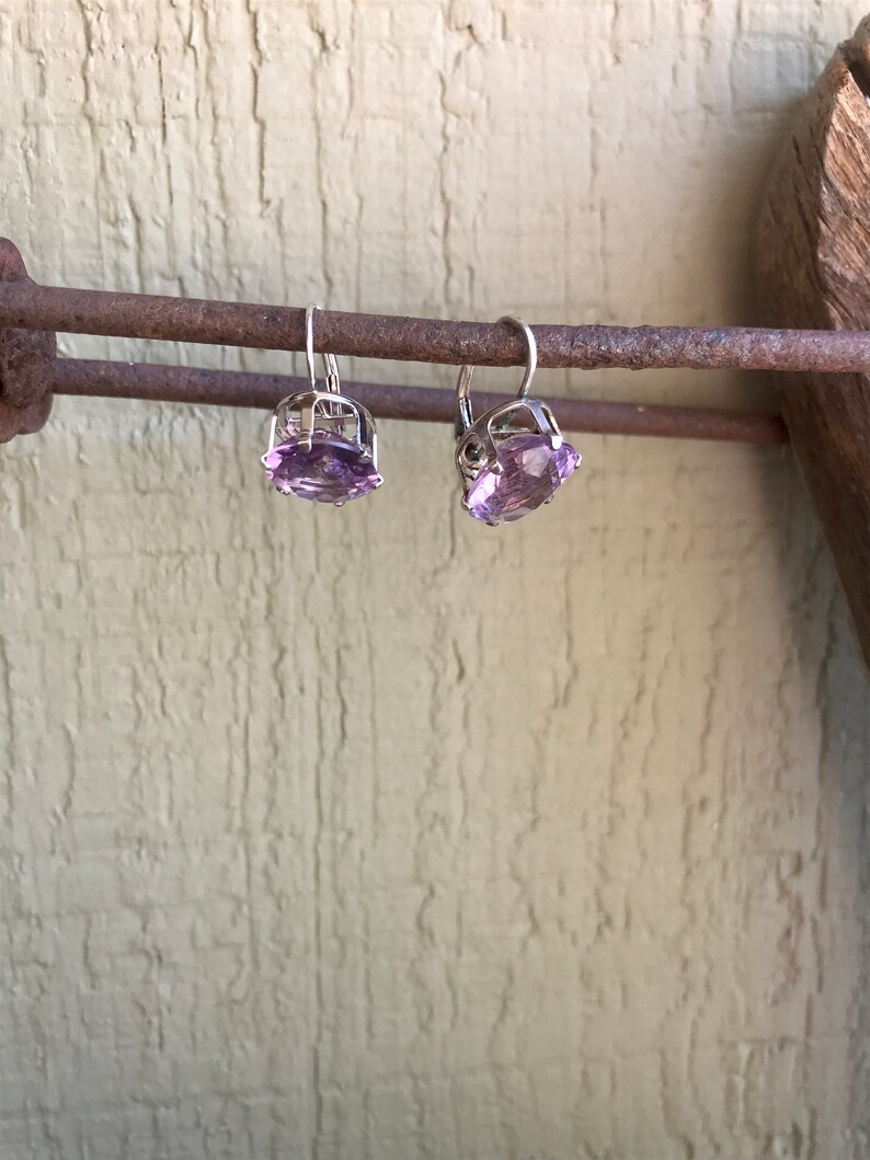 May include: A pair of silver earrings with amethyst gemstones. The earrings are hanging from a rusty metal bar.