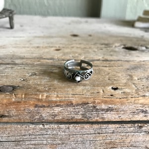 May include: A silver ring with a delicate floral design and a white pearl in the center.