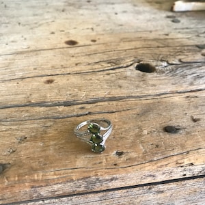May include: A silver ring with three green gemstones set in a V-shaped design.
