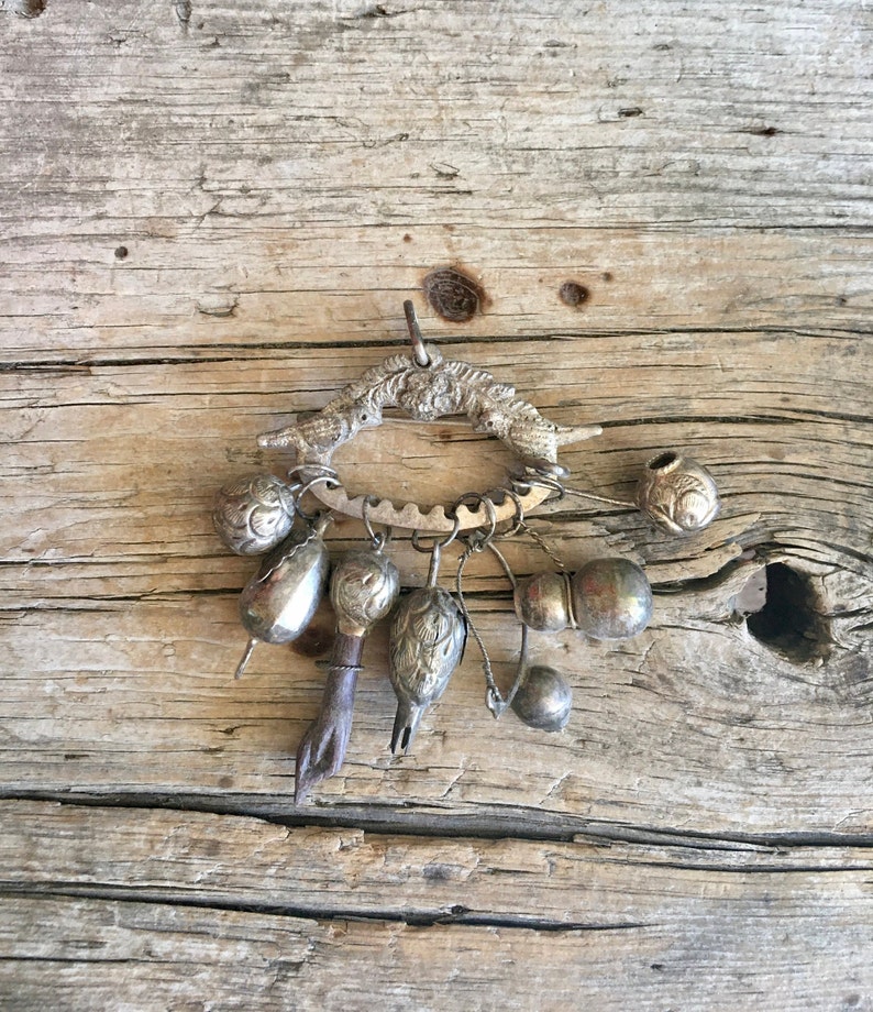 May include: A silver charm bracelet with a variety of charms, including bells, beads, and a small bird. The bracelet is hanging from a wooden surface.