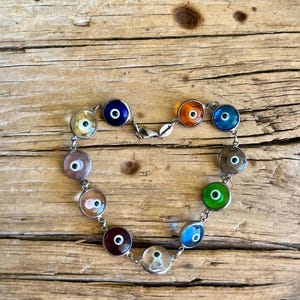 May include: A silver bracelet with a heart shape formed by the evil eye charms. The charms are round and feature different colored glass with blue eyes.