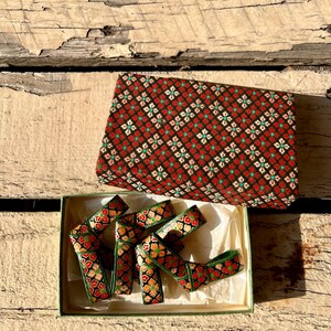 Peut inclure: Un ensemble de rubans décoratifs à motifs floraux dans une boîte. Le ruban présente un fond noir avec des fleurs rouges et oranges et des accents verts. La boîte a un motif floral rouge et noir assorti.