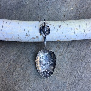 May include: A silver spoon with an ornate handle and a detailed design of a scene with a sun, a shepherd, and sheep on the bowl.
