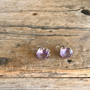 May include: A pair of silver earrings with purple gemstone accents. The earrings are on a wooden surface.