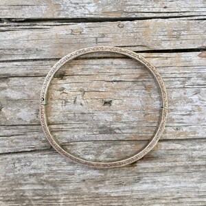 May include: A silver bangle bracelet with an intricate floral design. The bracelet is on a wooden surface.