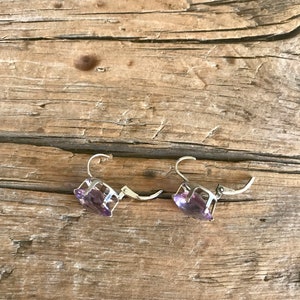 May include: A pair of silver earrings with purple gemstone accents. The earrings are on a wooden surface.