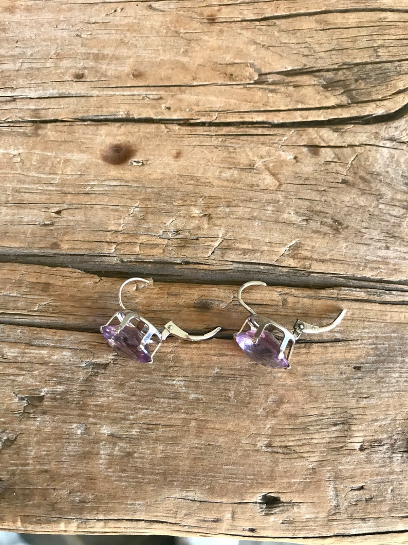 May include: A pair of silver earrings with purple gemstone accents. The earrings are on a wooden surface.