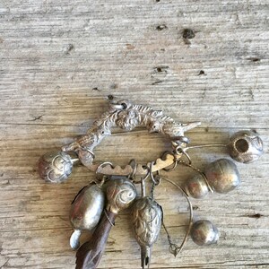 May include: A silver charm bracelet with a variety of charms, including bells, a bird, and a small wooden figure. The bracelet is on a wooden background.